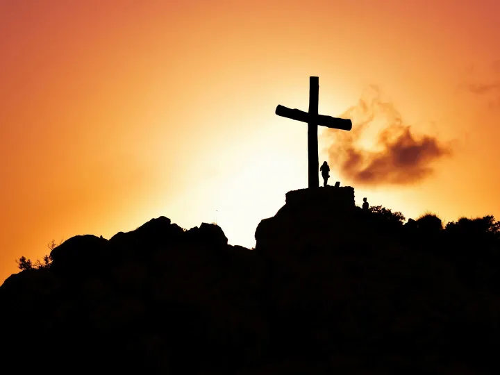 Majestic silhouette of a cross on a hill during a vivid sunset, symbolizing spirituality.