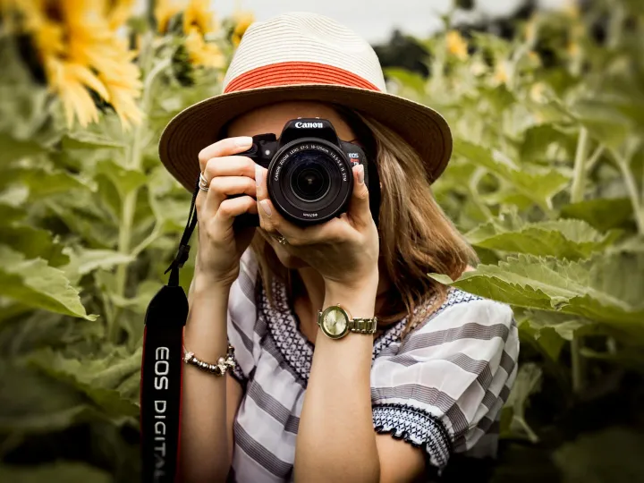 Woman with hat photographing sunflowers in a summe