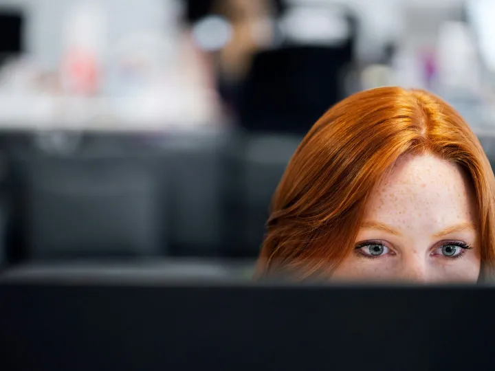 A woman with red hair intensely focused on a compu